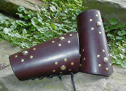 High Chivalry Bracers shown in very dark brown leather. Studs are brass double cap rivets with a nickel mount, pierced by a brass stud, at the center of the pattern. Hand creased edges provide a handsome trim.